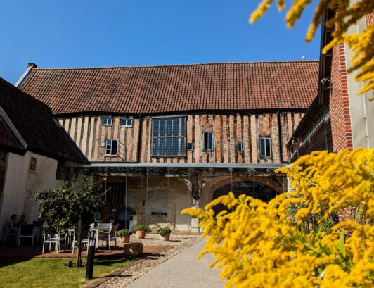 Medieval building Dragon Hall and outside area with table, chairs and mimosa