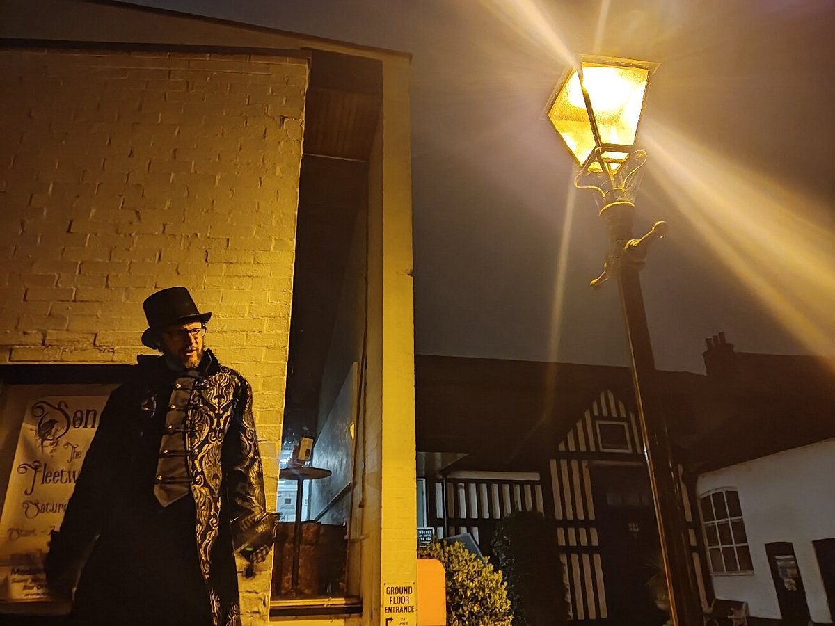 A man in a trench coat and top hat stands in front of an old theatre
